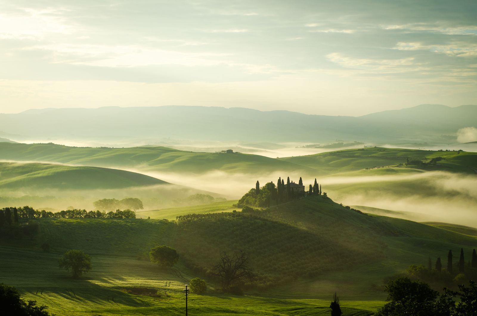 Colline della Val d'Orcia nella nebbia del mattino, con un casale sulla collina